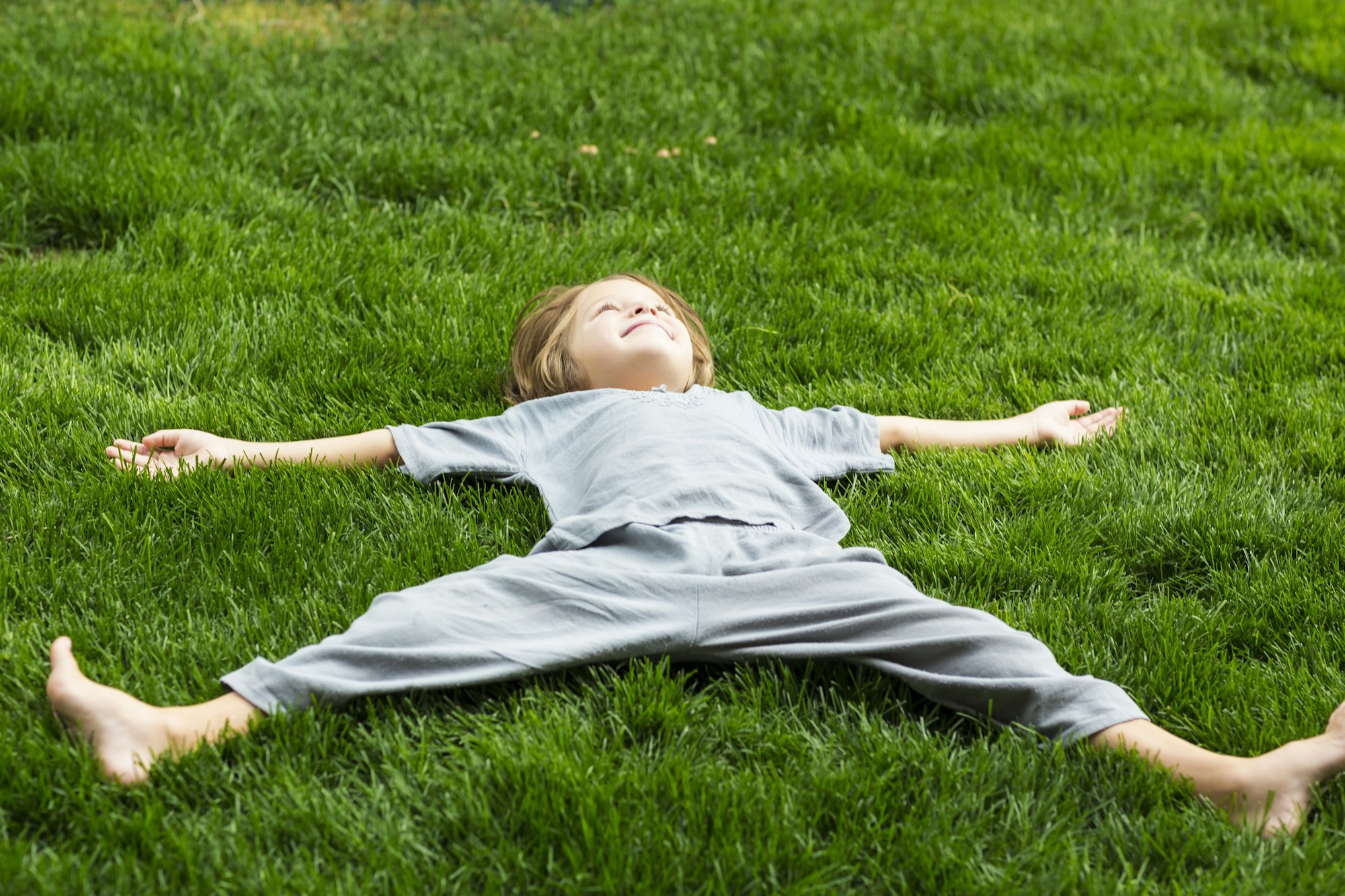 5 year old boy lying down on lush green lawn looking up