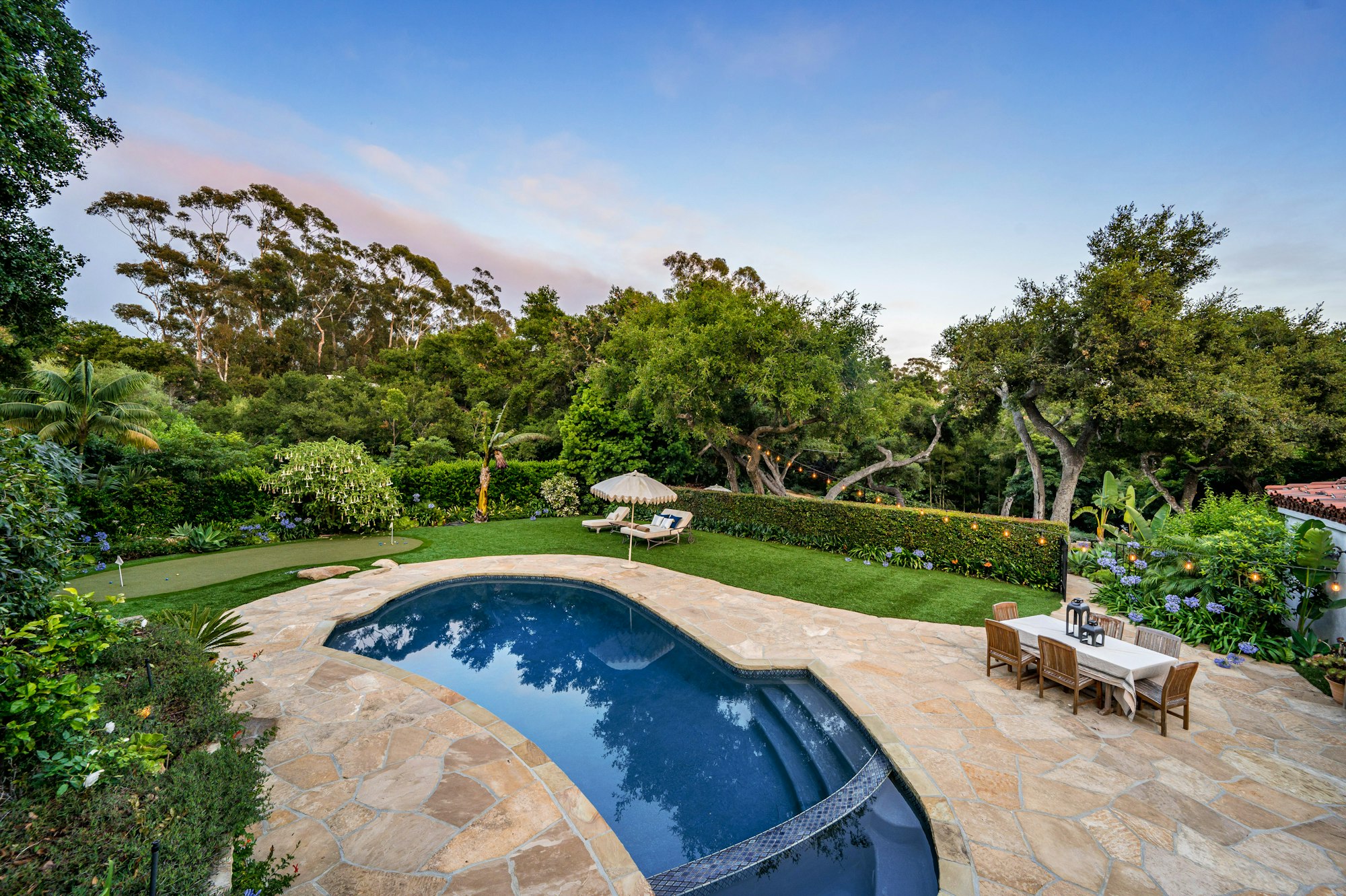 a backyard with a swimming pool and trees, plants and edged lawn