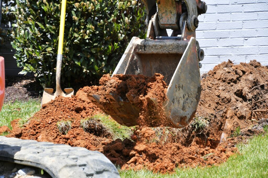 Backhoe digging dirt in lawn to install electrical & gas lines. Digging hole in yard. Scoopful soil